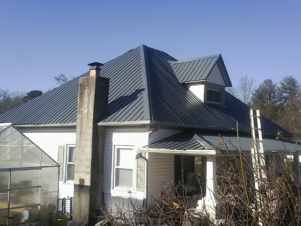 Dark blue standing seam metal roof on a white farmhouse with dormer — Slate & Tile Roof Repair by Roofing Brothers in Comfort