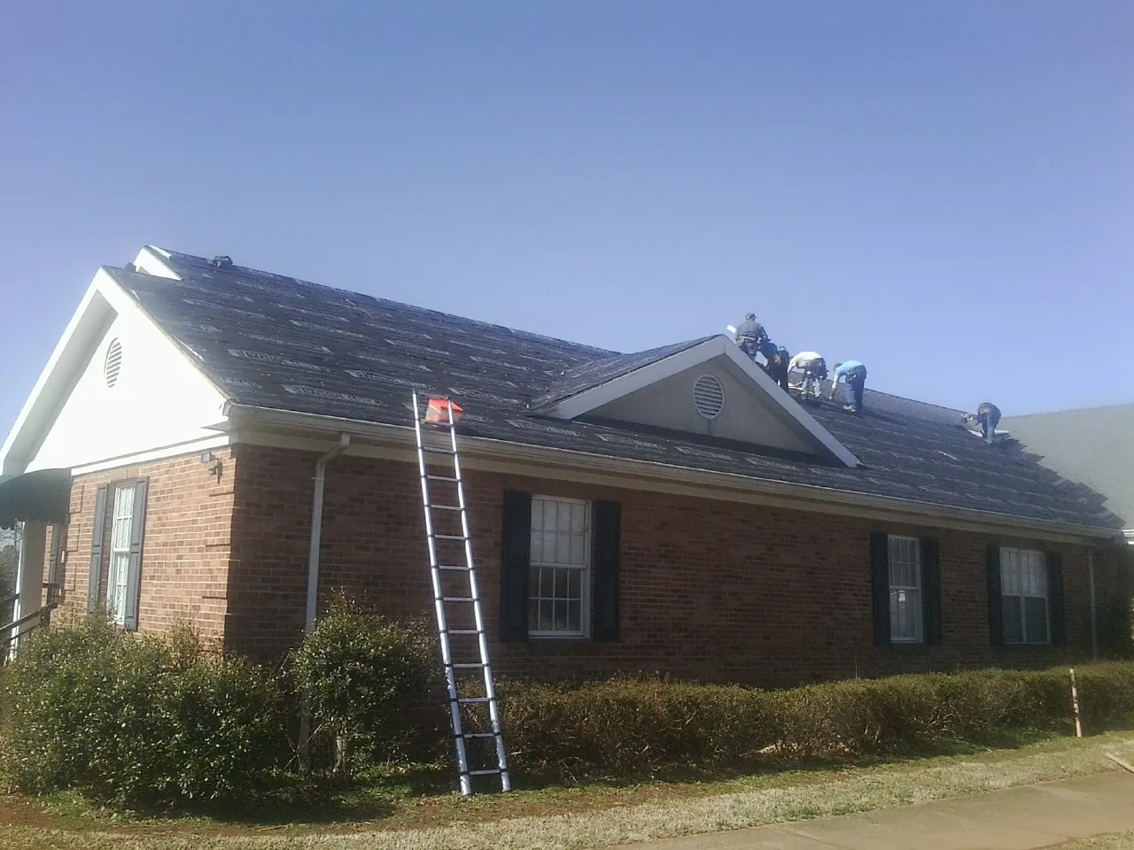 Crew tearing shingles off a brick ranch roof with a ladder set — Metal Roof Repair work by our crew in Comfort