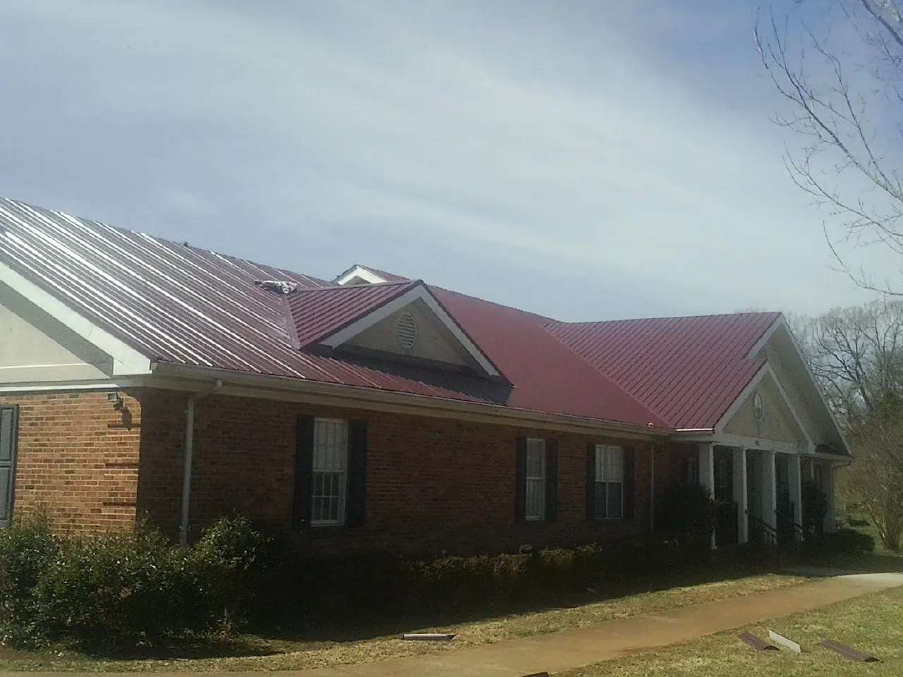 Red metal roof with gabled entries on a long brick building, from a Hail Damage Roof Repair job in Comfort