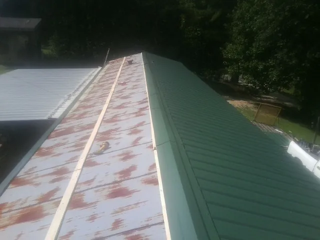 Old rusted panels beside newly installed green metal roofing — Wind Damage Roof Repair by Roofing Brothers in Comfort