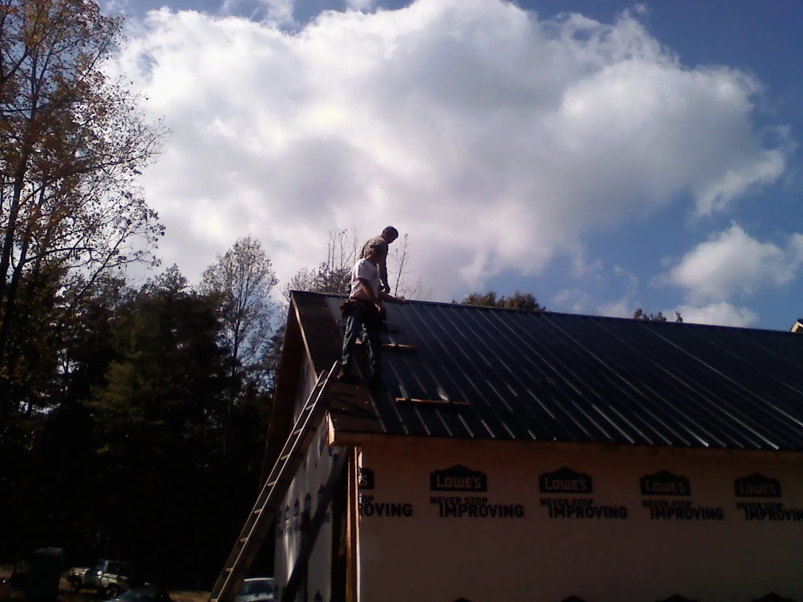 Roofer fastening dark metal panels high against a cloudy sky, from a Roof Inspection job in Comfort