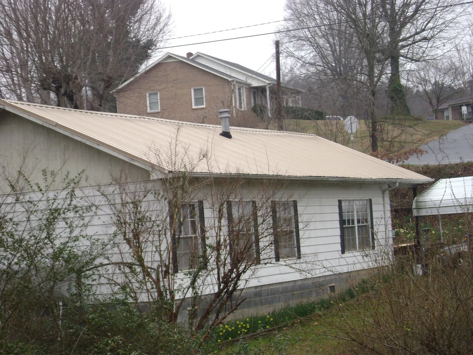 Tan metal roof on a white sided house set into a hillside — Commercial Roofing by Roofing Brothers in Comfort